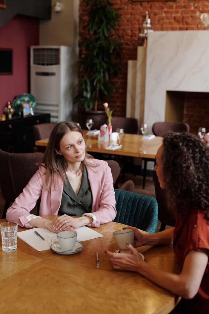 Two women having a thoughtful conversation in a cozy café setting, discussing over coffee.