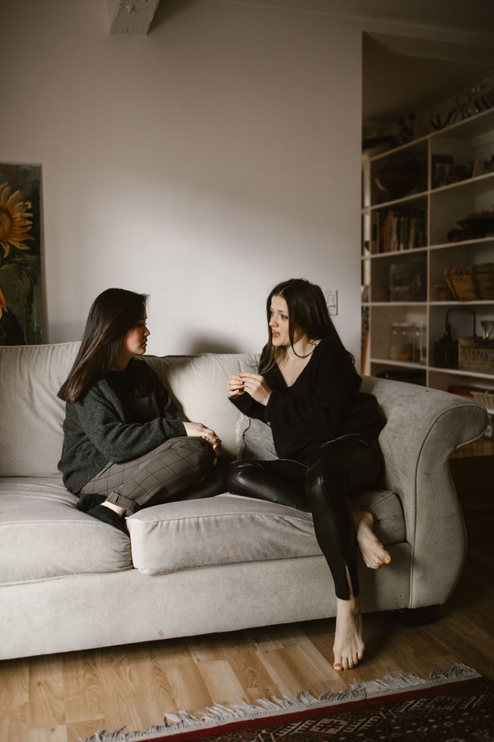 Two women sitting on a sofa sharing a thoughtful conversation in a cozy home setting.