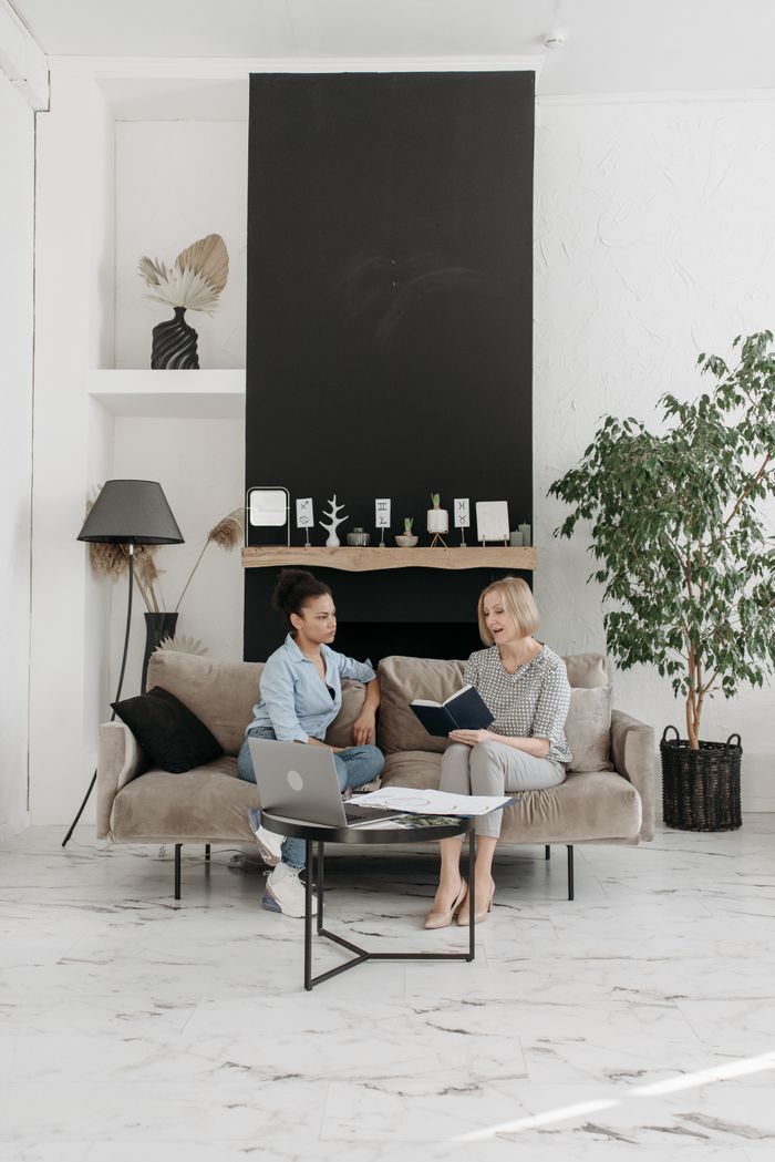 Two women engaged in a cozy conversation in an elegantly designed minimalist living room.